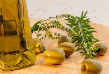 Aceite de oliva en un recipiente de vidrio acompañado de olivas y romero, un ingrediente ideal para conservar ensaladas.