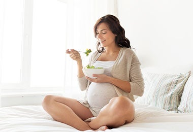 Mujer embarazada comiendo una ensalada, muestra de alimentación en el embarazo basada en ingredientes naturales
