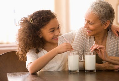 Niña y abuela compartiendo un vaso de leche en casa, una escena cotidiana con alimentos con calcio