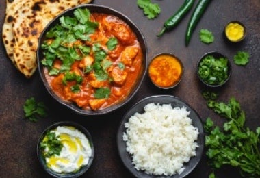 Plato de Butter Chicken con arroz basmati, naan y chutneys, sobre un fondo oscuro