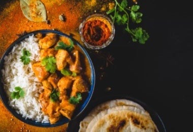 Bowl de Butter Chicken servido con arroz y naan, acompañado de especias