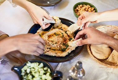 Amigos compartiendo hummus con pan pita, dos comidas mediterráneas. 