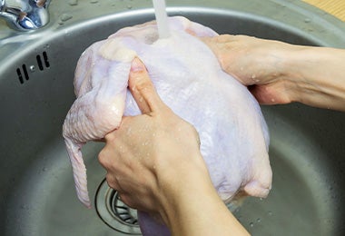 Un pollo entero siendo lavado con agua.