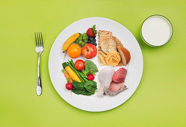 Un plato con verduras, frutas, carnes, pastas y otras comidas para una dieta balanceada con proteínas magras