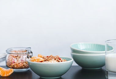 Tazón de granola y trozos de mandarina acompañado de un vaso de leche, una opción de desayuno que representa los alimentos con omega 3