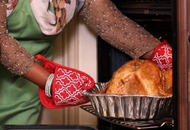 Mujer sacando pollo del horno utilizando guantes y agarraderas de cocina  
