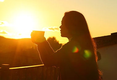 Mujer disfrutando de una aguapanela en su casa mientras ve el paisaje de la mañana