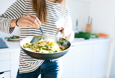 Una mujer salteando unos noodles con verduras. 