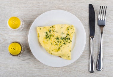 Omelette con hierbas, un salero y cubiertos, un desayuno con alta carga de nutrientes.