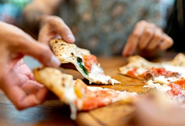 Personas comiendo porciones de pizza de masa delgada