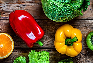 Un pimiento rojo y uno amarillo, acompañados de otras frutas y verduras.