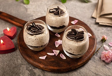 Postre de chocolate y galletas en vaso, sobre una bandeja decorada con pétalos. 