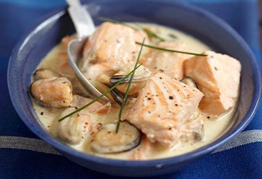 Primer plano de un tazón con trozos de salmón y mejillones en salsa cremosa, mostrando alimentos con vitamina D