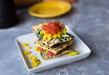 Tostadas triangulares cubiertas con mezcla de atún, aguacate, pimiento y semillas de sésamo negro, representando alimentos con vitamina D