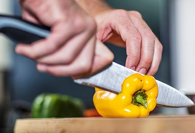 Una persona cortando un pimiento con un cuchillo, un utensilio clave para un asado. 