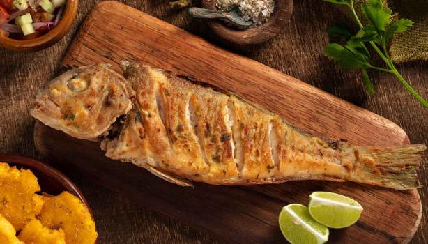 Un pescado frito entero, servido sobre una tabla y acompañado con limón. 