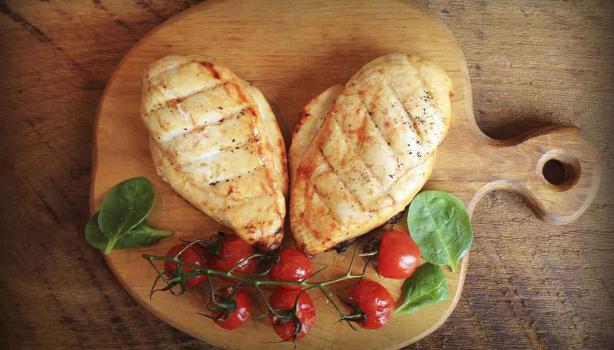 Dos pechugas de pollo con un racimo de tomates cherry, una comida con proteínas magras encima de una tabla