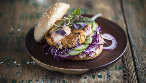 Apetitosa hamburguesa de pescado con vegetales emplatada y sobre una mesa de madera-