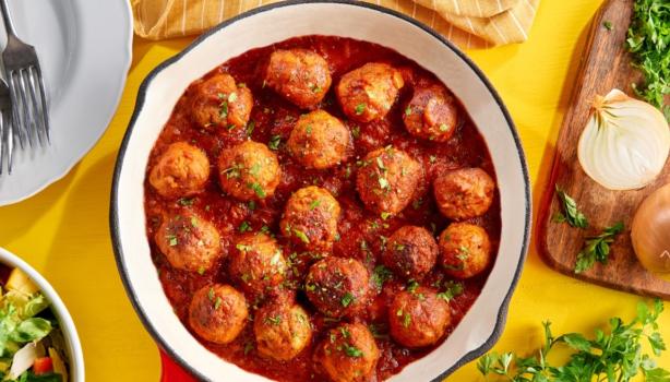 Albóndigas caseras en salsa putanesca servidas en una sartén con cebollas y cilantro