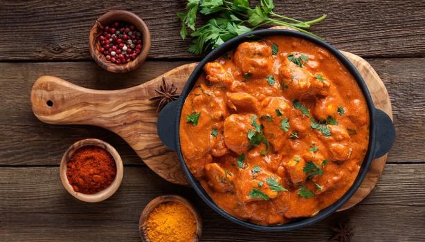 Butter Chicken con cilantro y acompañado de especias sobre tabla de madera