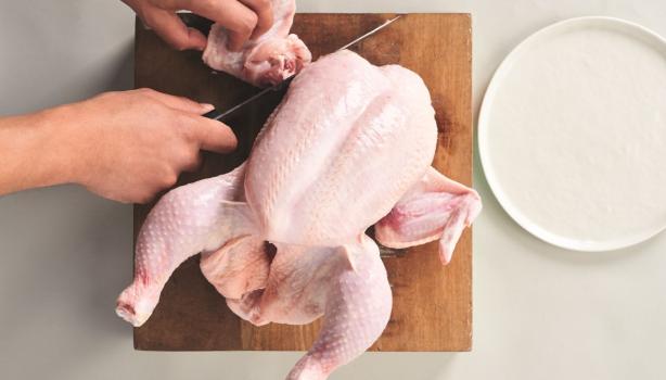 Corte de la carcasa de pollo sobre una tabla de madera, ideal para usar en caldos de hueso de pollo
