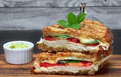 Pan panini relleno de jamón, tomate y albahaca, acompañado con salsa 