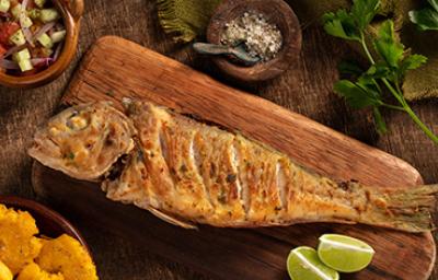 Un pescado frito entero, servido sobre una tabla y acompañado con limón. 
