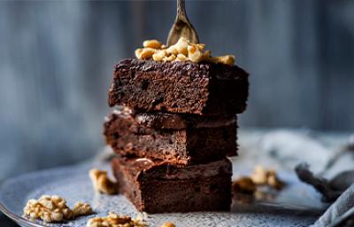 Plato con tres pisos de brownie espolvoreado con nueces, este es un postre sin gluten