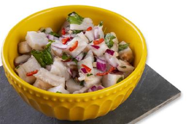 Ceviche con leche de tigre, cebolla morada, culantro y limón en un recipiente amarillo sobre un fondo blanco