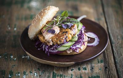 Apetitosa hamburguesa de pescado con vegetales emplatada y sobre una mesa de madera-