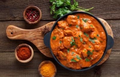 Butter Chicken en estilo rústico con especias aromáticas Butter Chicken con cilantro y acompañado de especias sobre tabla de madera