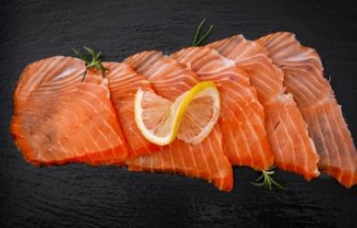 Salmón ahumando en frío, un delicioso manjar. Pequeños trozos de salmón ahumado frío sobre fondo negro.