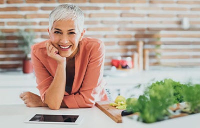 Mujer con tabla a su lado llena de fruta en trozos, representando un momento cotidiano de alimentación en el adulto mayor