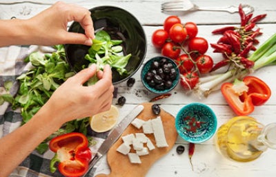 Vista superior de una persona preparando una ensalada fresca con lechuga, tomates cherry, pimientos y queso en dados