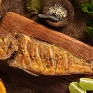 Un pescado frito entero, servido sobre una tabla y acompañado con limón. 