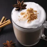 Bebida caliente con leche, canela y anís en una taza de vidrio grueso en una toma en picado