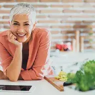 Mujer con tabla a su lado llena de fruta en trozos, representando un momento cotidiano de alimentación en el adulto mayor