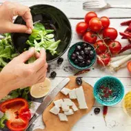 Vista superior de una persona preparando una ensalada fresca con lechuga, tomates cherry, pimientos y queso en dados