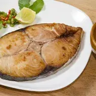 Un filete de pescado dorado y jugoso servido en un plato blanco con rodajas de limón y hojas frescas