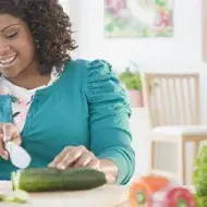 Una mujer sonríe mientras corta un pepino en una tabla de madera en la cocina