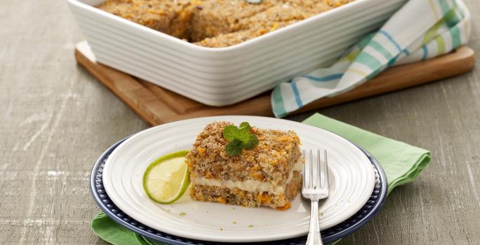 Fotografía en tonos de verde sobre un banco de madera gris, una tabla de cortar de madera, un paño de cocina verde, uno rayado en verde. En el centro, un plato redondo blanco con un trozo de kebab relleno. Al fondo, un refractario con toda la kibbeh.